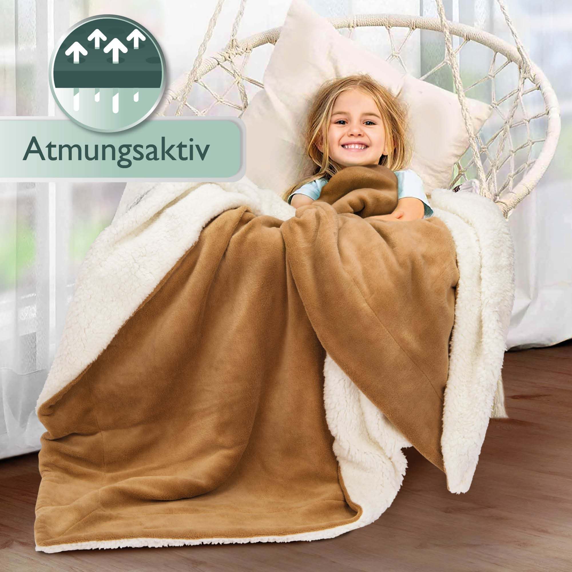 Beautissu Sherpa Kuscheldecke Alina in beige covering a child on a chair, 150x200cm/220x240cm sizes, soft microfibre polyester, warm and breathable.