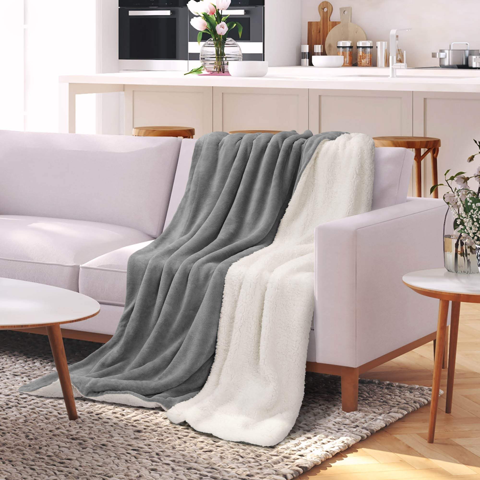 Beautissu Sherpa Kuscheldecke Alina draped over a sofa, showcasing its plush, dual-textured design in gray and white fleece.