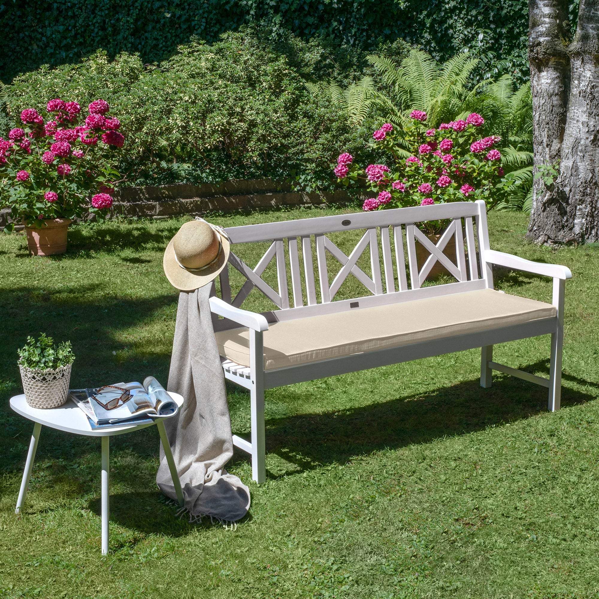 Beautissu Base BK bench cushion on garden bench surrounded by flowers, showcasing comfort and style.