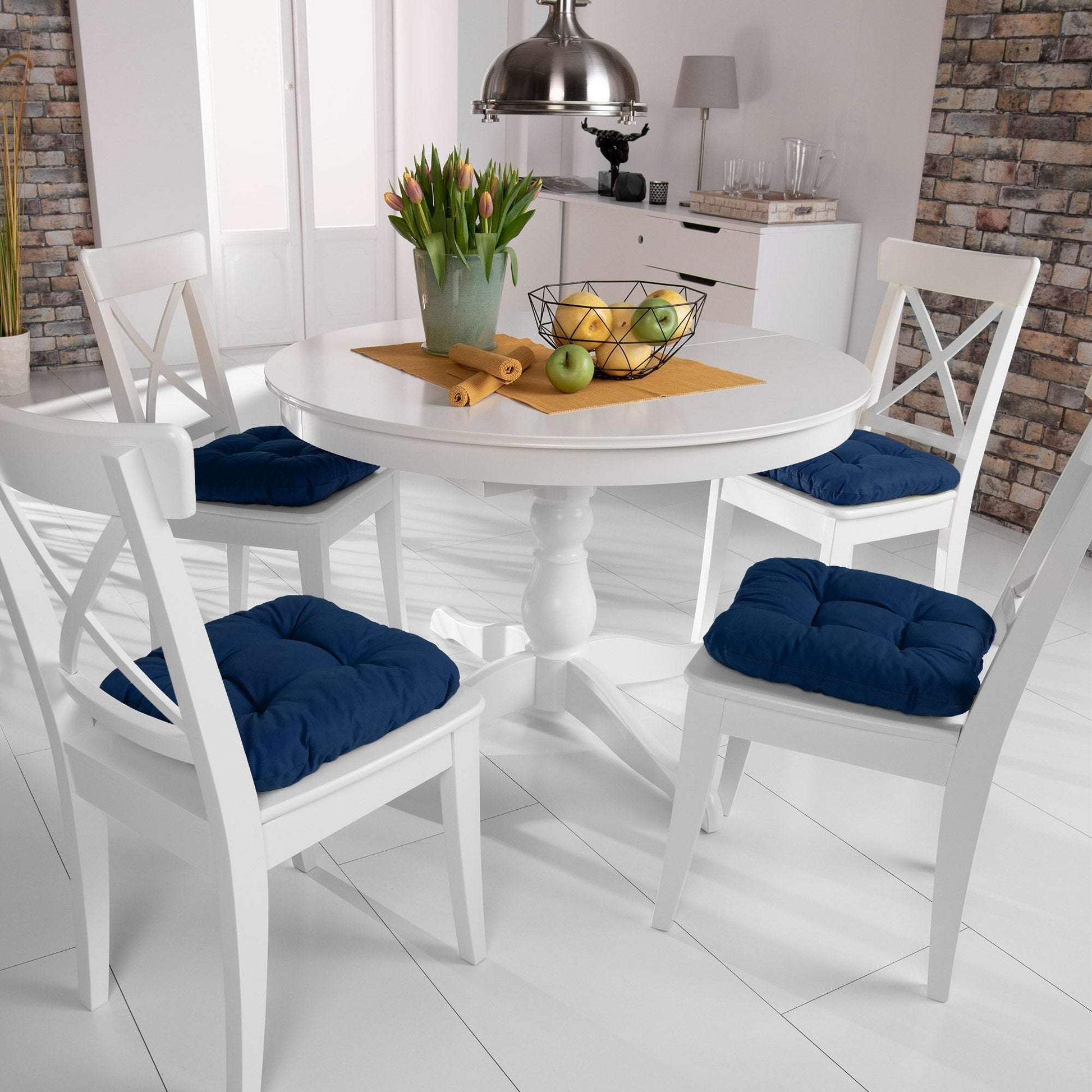 4er Set Beautissu Lisa Stuhlkissen 40x40cm in blue on dining chairs around a white table in a bright kitchen.