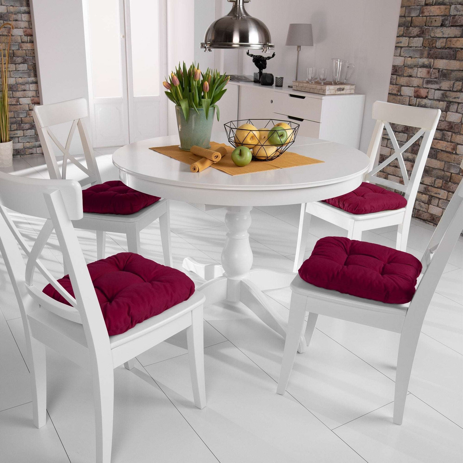 4er Set Beautissu Lisa chair cushions in diverse colors on white chairs around a dining table.
