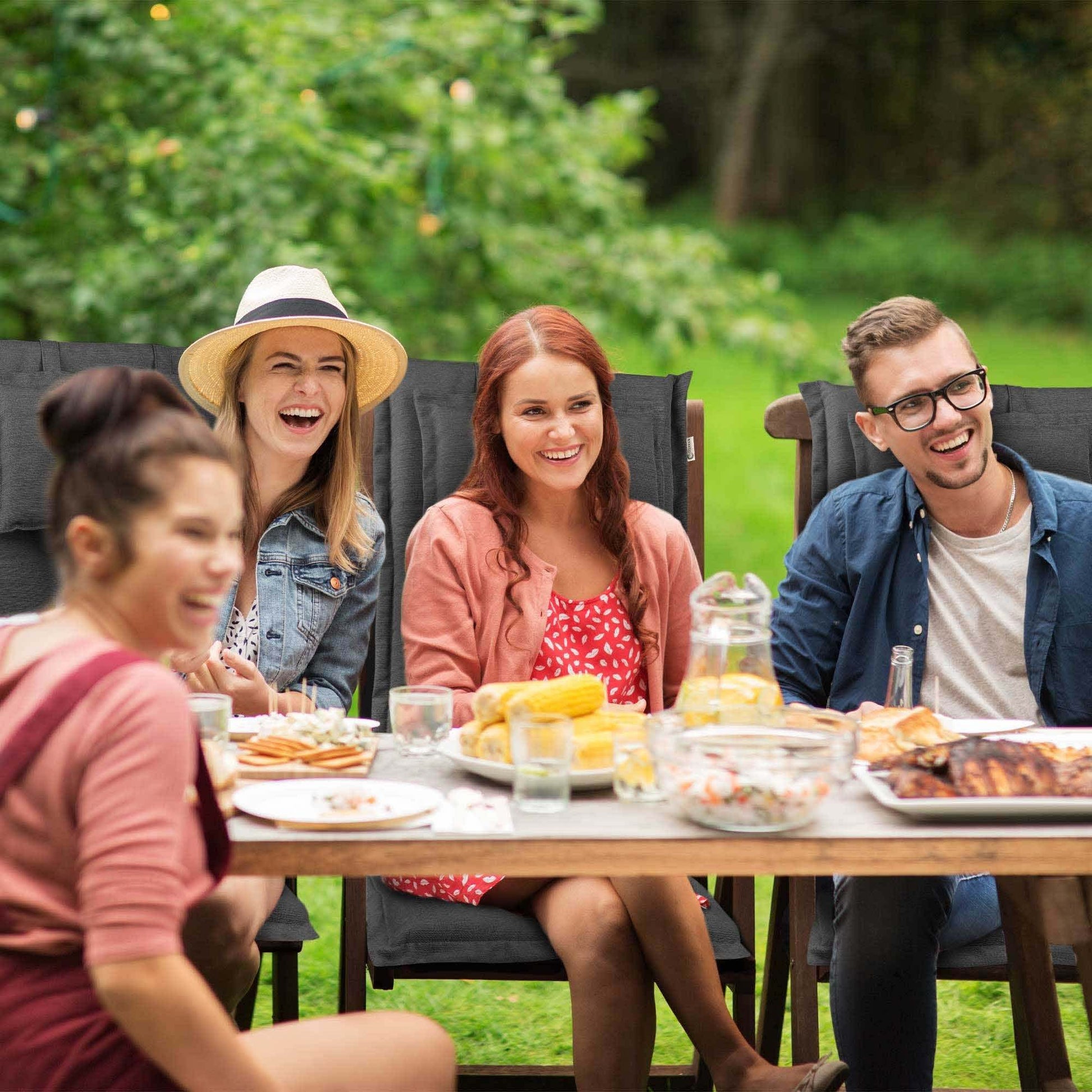 Group of people enjoying an outdoor meal with Beautissu HighLux garden chair cushions.